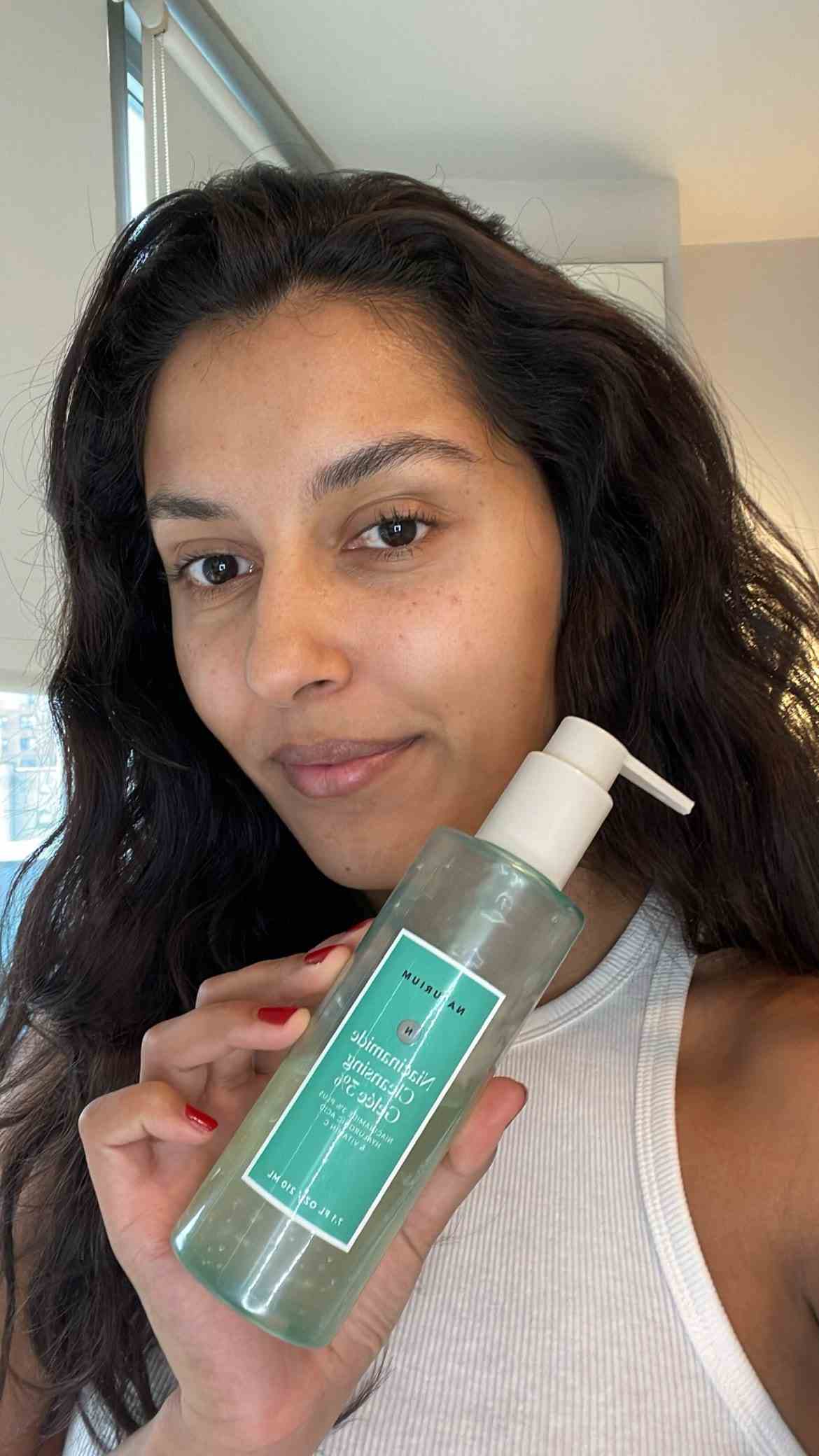A selfie of Allure editorial assistant Talia Gutierrez with fresh clean skin and holding the Naturium Niacinamide...