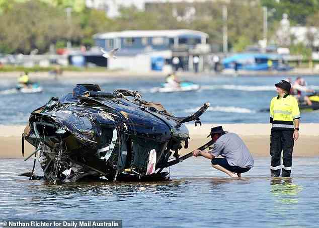 The man inspects the interior of the wrecked Sea World helicopter on Tuesday as crews worked on recovering the remnants