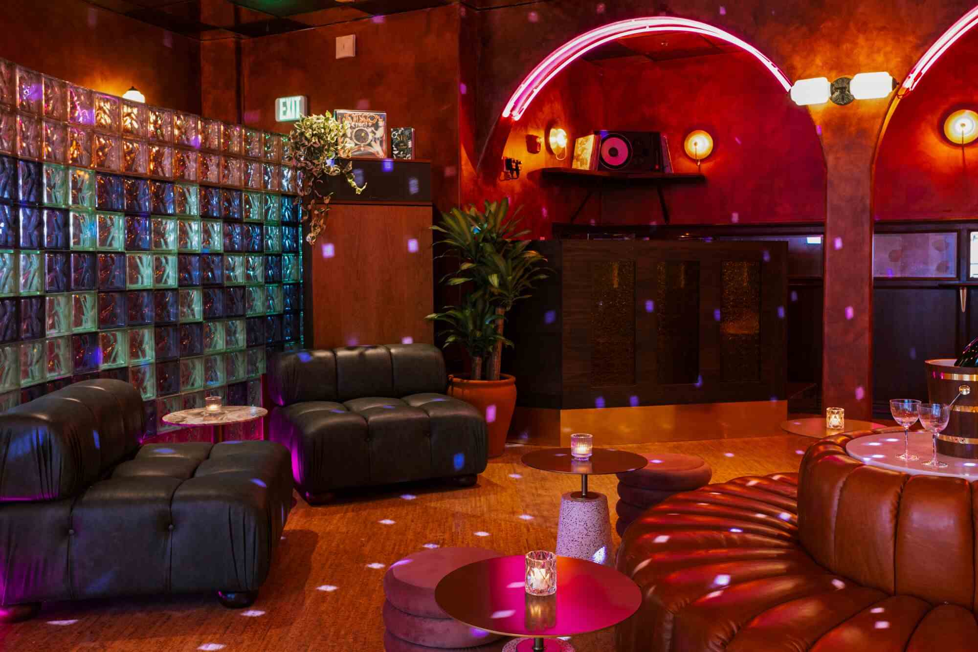 Ein dunkles Bar-Interieur mit Ledersitzen, rosa Neon über den Torbögen und einer Wand aus Glasbausteinen an einem Ende.