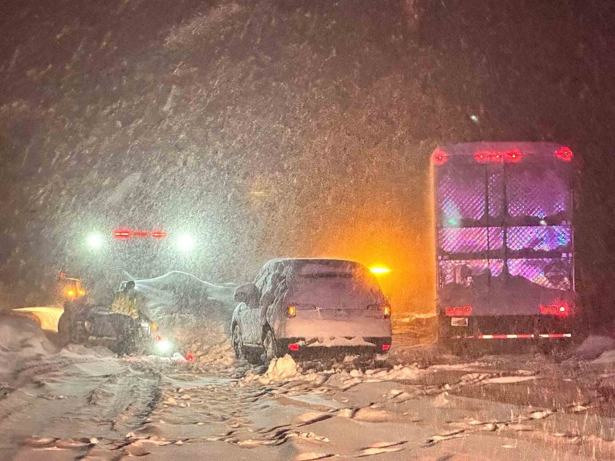 Ein Auto und ein Lastwagen stehen am Straßenrand, während nachts noch Schnee fällt.