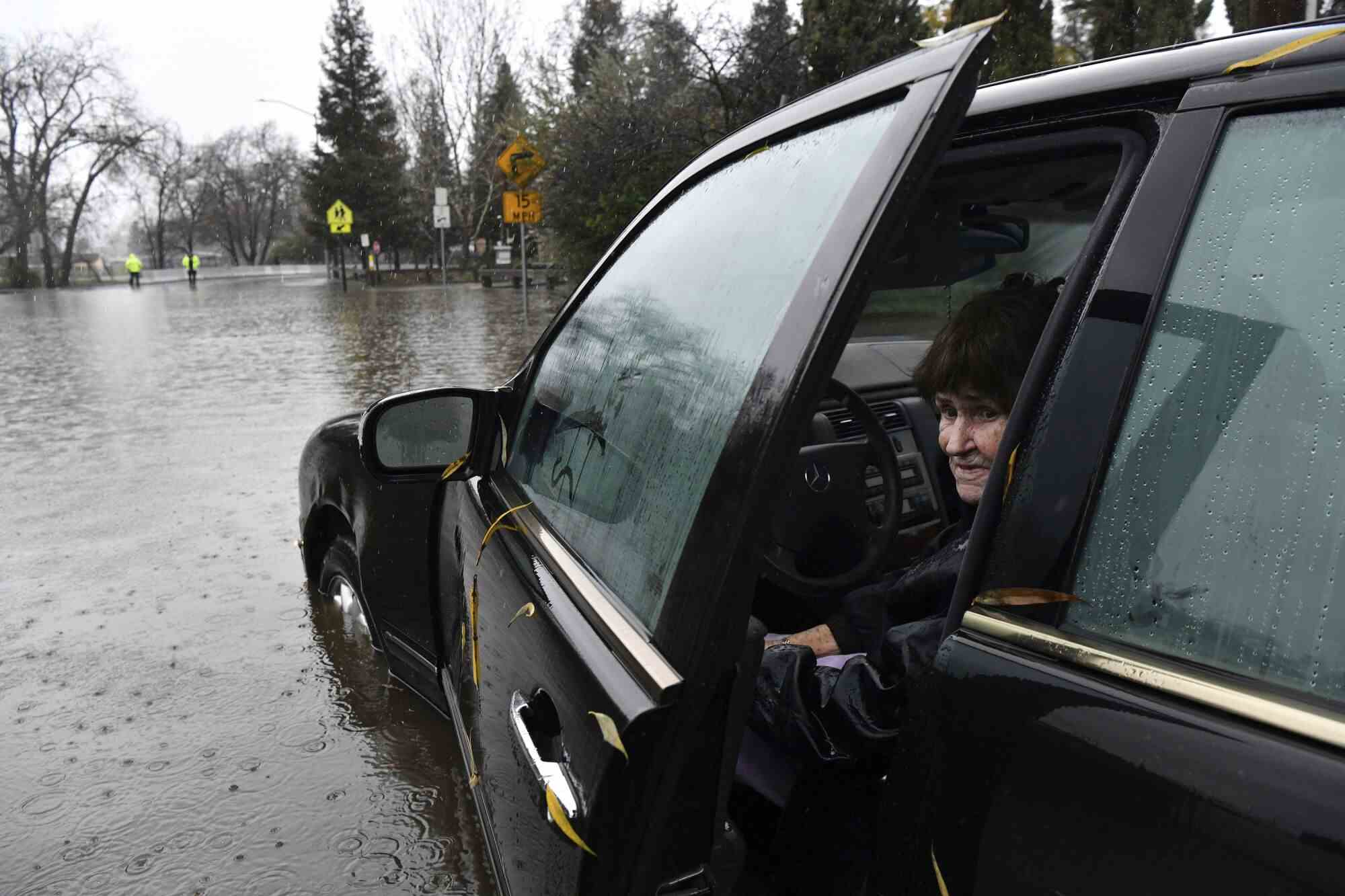 Eine Frau lugt aus einer offenen Tür ihres Autos, das in einem überschwemmten Gebiet steht.