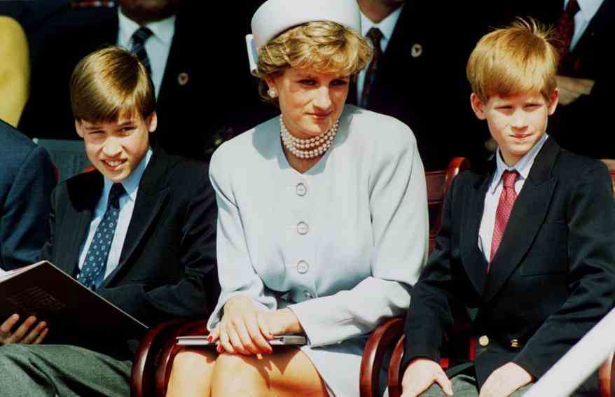 Prinzessin Diana sitzt zwischen Prinz Harry und Prinz William im Anzug