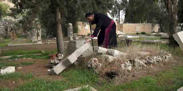 Hosam Naoum, ein palästinensischer anglikanischer Bischof, berührt am Mittwoch, den 4. Januar 2023, ein beschädigtes Grab, auf dem Vandalen mehr als 30 Gräber auf einem historischen protestantischen Friedhof auf dem Berg Zion in Jerusalem entweiht haben.
