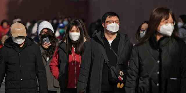 Menschen mit Gesichtsmasken gehen am Freitag, 6. Januar 2023, eine Straße in Peking entlang. 