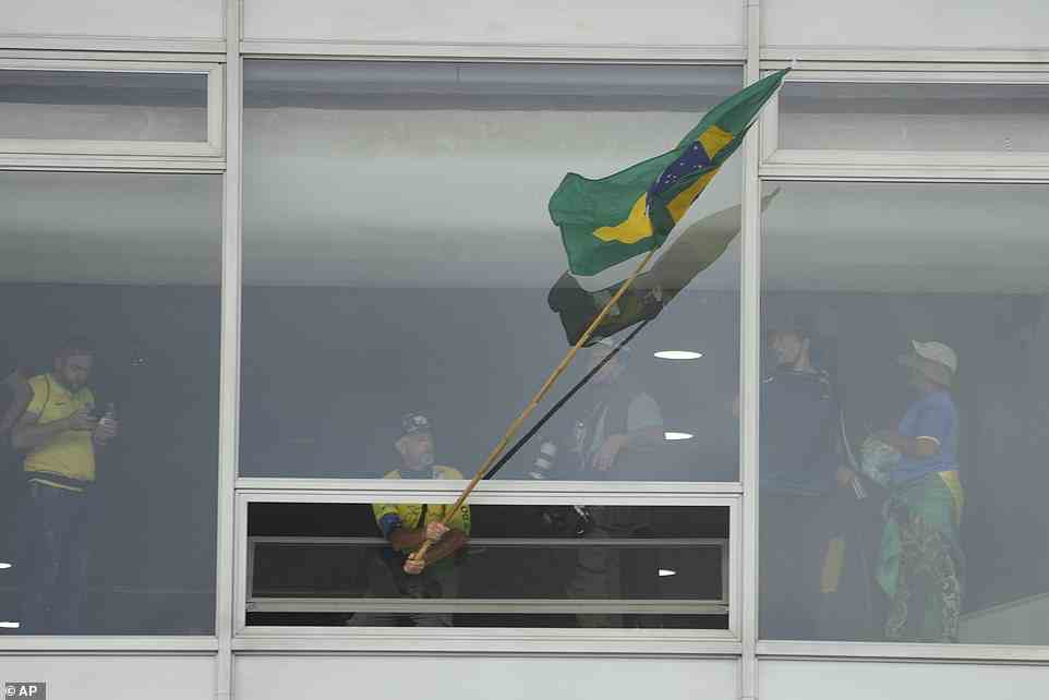 Ein Mann schwenkt eine brasilianische Flagge aus dem Fenster des Regierungsgebäudes.  Die Farben sind zum Synonym für das Bolsonaro-Regime geworden