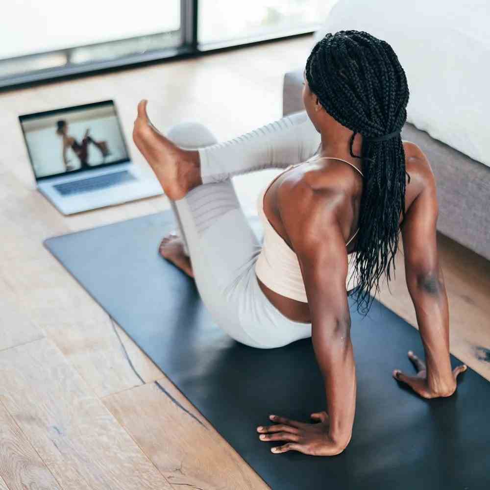 Alo Moves (monatliches Abonnement) Model mit dem Blick von der Kamera abgewandt beim Yoga vor einem Computerbildschirm im Schlafzimmer