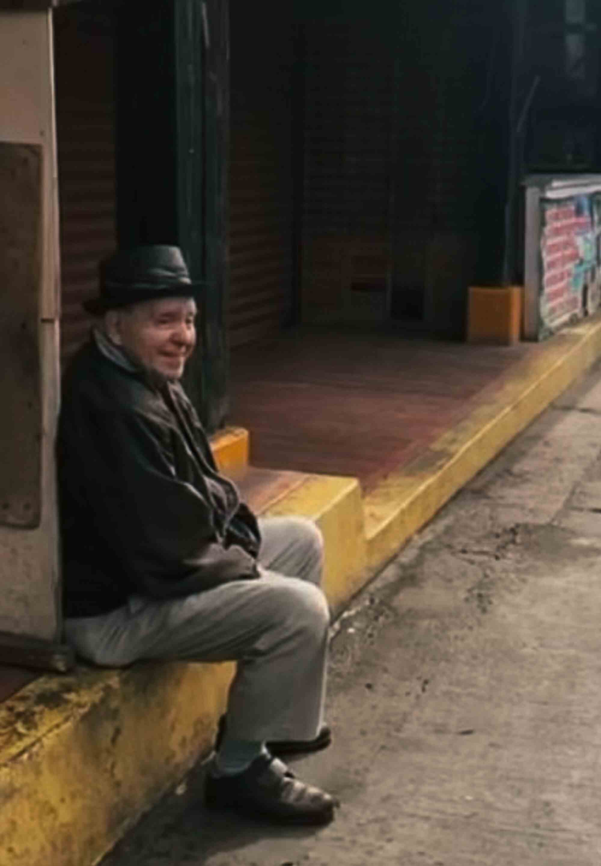 Ein älterer Mann sitzt und lächelt auf einem Bordstein