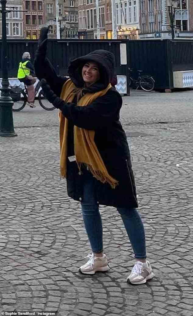 Touristin: Die Brünette strahlte vor dem Belfried von Brügge, während sie scherzhaft ihre Hände hochhielt, um so zu tun, als würde sie den Glockenturm halten