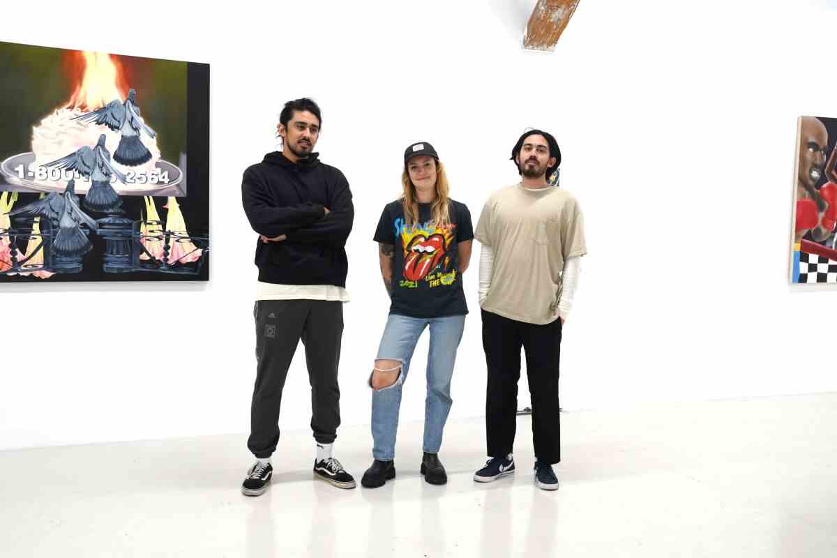 Drei Personen stehen neben einem Kunstwerk, das in der Good Mother Gallery an der Wand hängt.