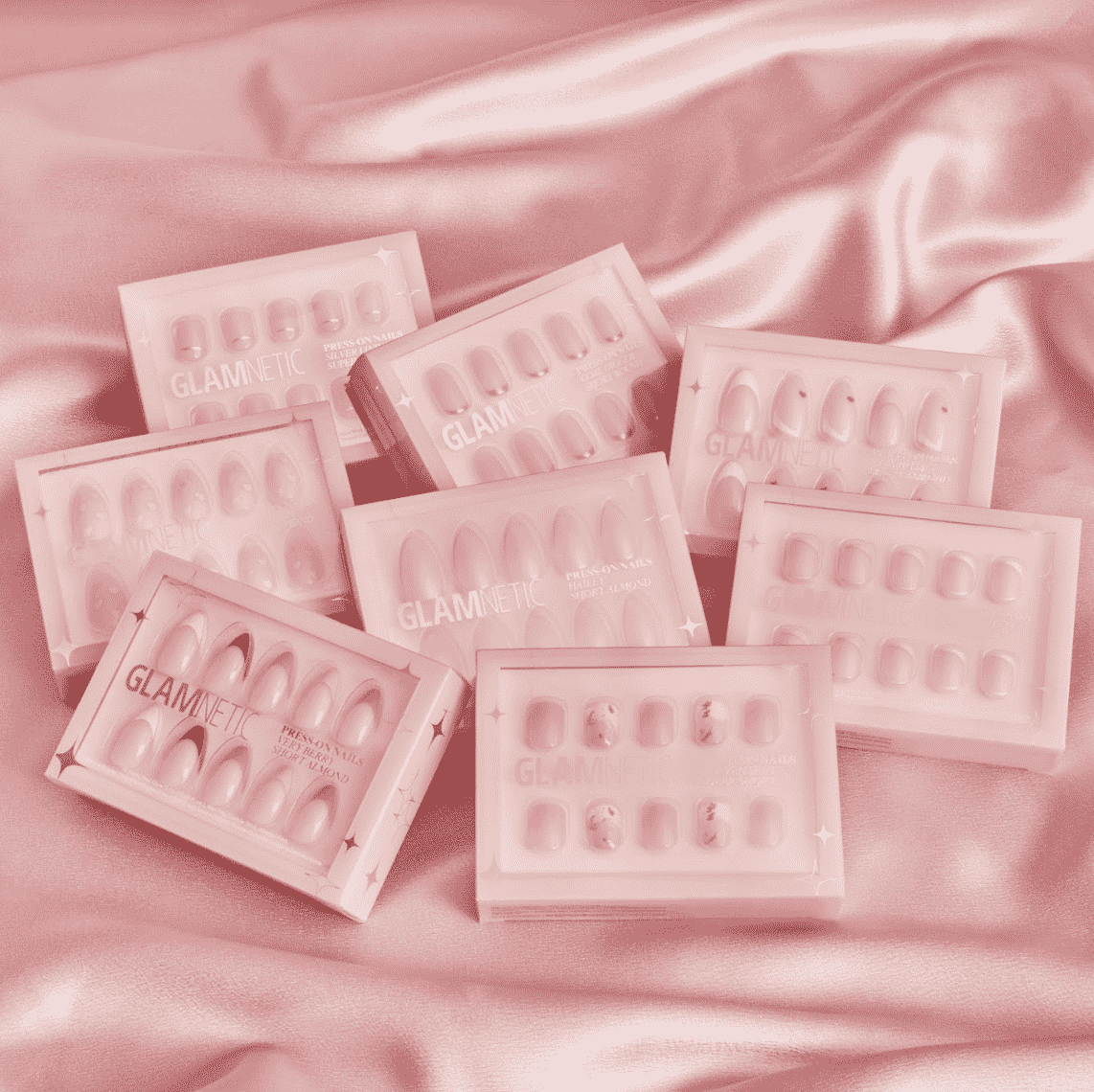 Glamnetic Short and Sweet Press-on Nail Collection rosa Schachteln mit Press-on-Nägeln auf rosa Seidenoberfläche