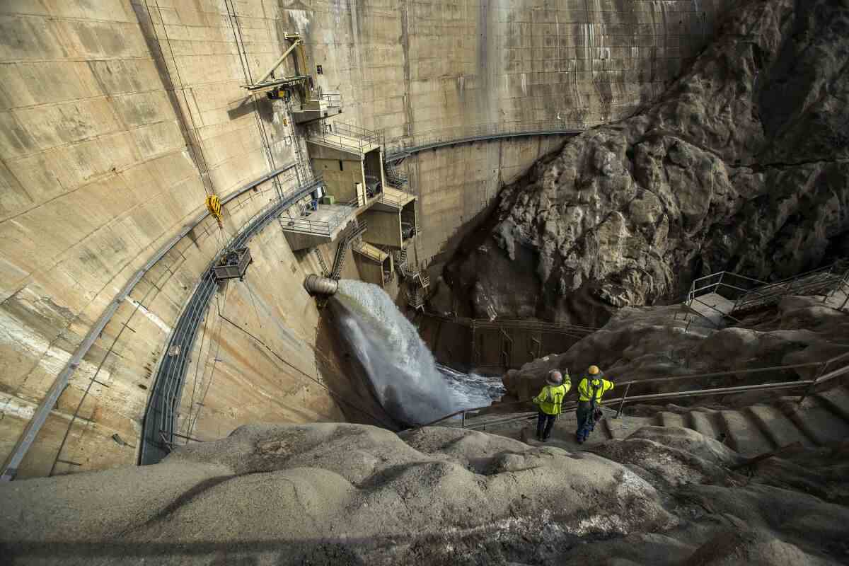 Zwei Arbeiter werden von der hoch aufragenden Wand eines Staudamms in den Schatten gestellt. 