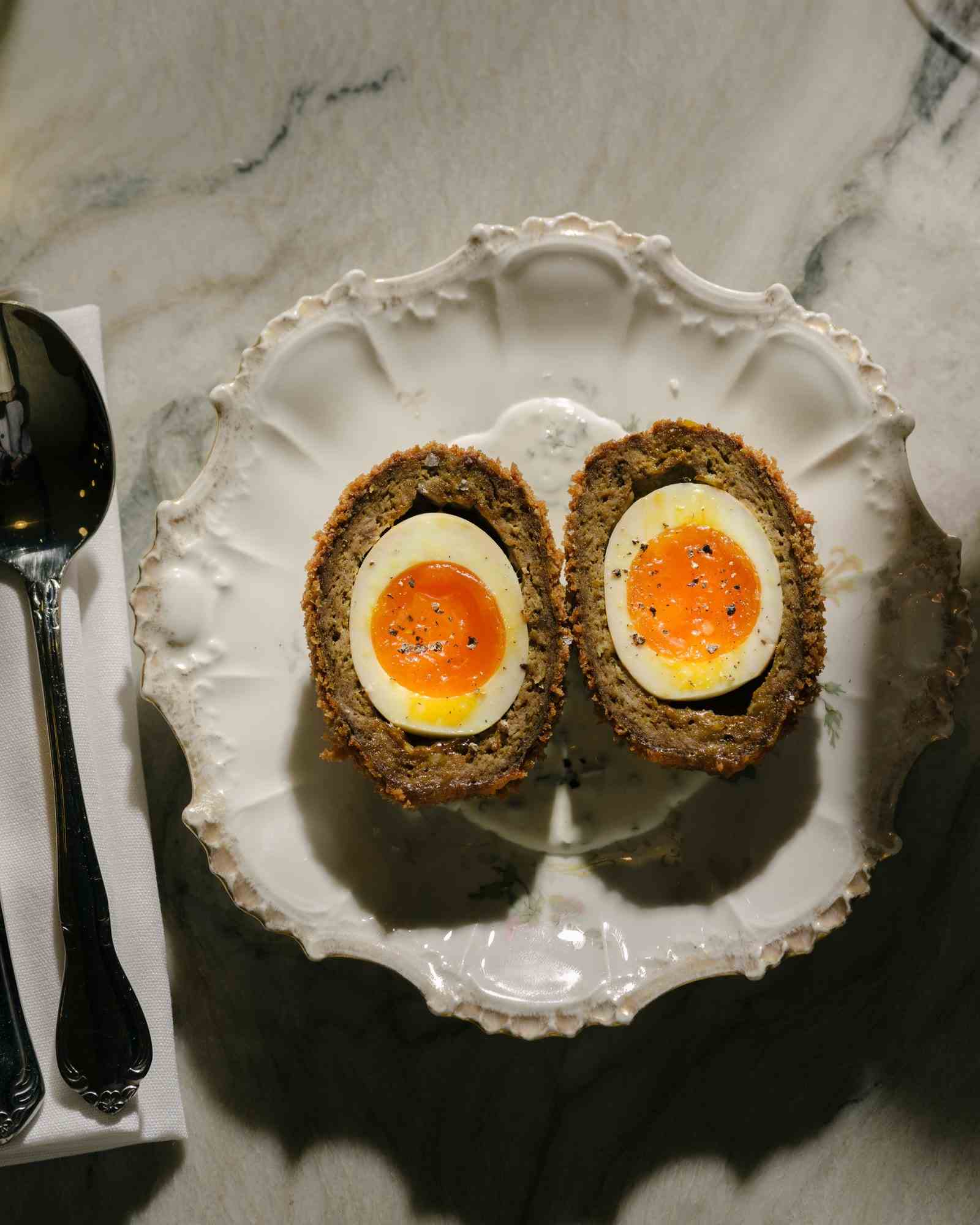 Ein halbiertes schottisches Ei liegt offen auf einem kleinen Teller.