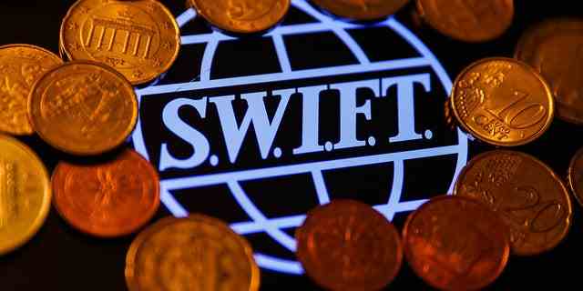 Das SWIFT-Logo (Society for Worldwide Interbank Financial Telecommunication), das auf einem Telefonbildschirm angezeigt wird, und Münzen sind auf diesem Illustrationsfoto zu sehen, das am 23. Januar 2022 in Krakau, Polen, aufgenommen wurde.