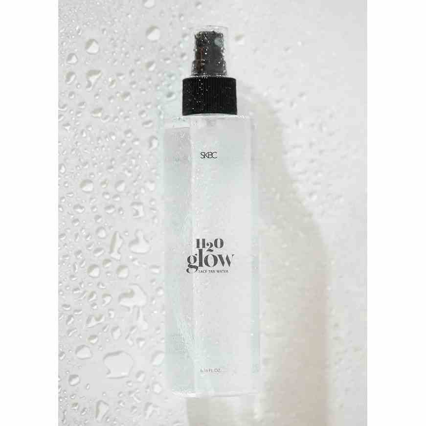 SKBC H20 Glow klare Sprühflasche mit schwarzer Düse auf grauem Hintergrund mit Wassertropfen und weißen Rändern