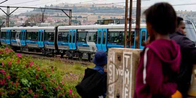 Fußgänger beobachten am Mittwoch, den 8. Februar 2023, einen Zug, der von Johannesburg nach Naledi in Soweto, Südafrika, fährt.