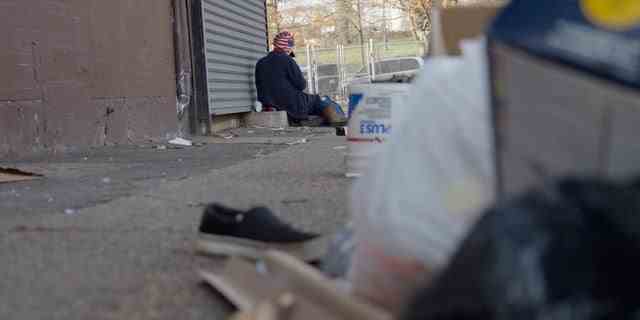 Ein Süchtiger sitzt an der Ecke in Kensington.  Der Vordergrund ist mit Müll und anderem Gerümpel übersät – ein alltäglicher Anblick in der Nachbarschaft von Philadelphia.
