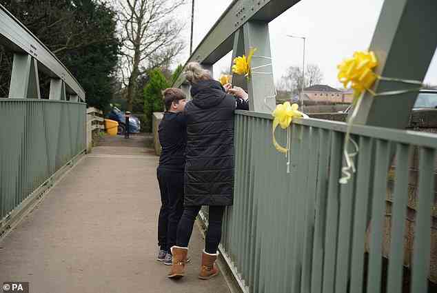 A woman and young boy tie a yellow ribbon bearing a message of hope to a bridge over the River Wyre in St Michael's on Wyre, Lancashire on Sunday