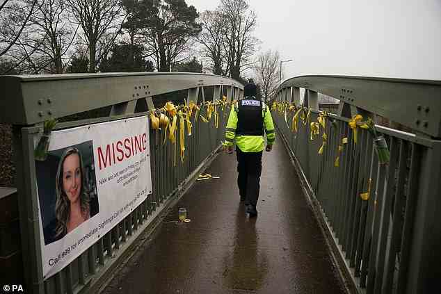 A police officer walks past a missing person appeal poster for Nicola Bulley and yellow ribbons and messages of hope tied to a bridge over the River Wyre in St Michael's on Wyre
