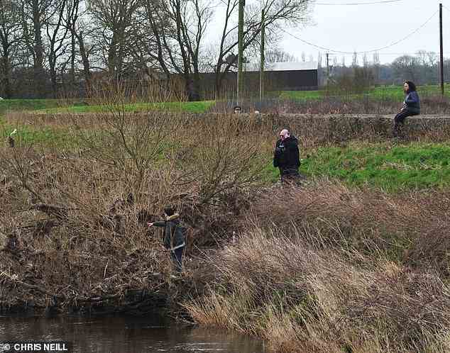 Ein Mitglied der Öffentlichkeit scheint heute auf eine Stelle im Unterholz am Fluss Wyre zu zeigen, während die Polizei zuschaut