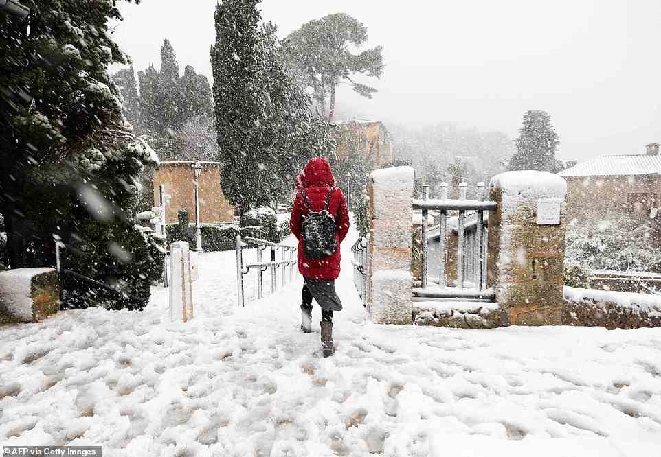 Eine Frau läuft am Montag bei starkem Schneefall eine schneebedeckte Straße im Bergdorf Valldemossa entlang