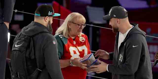Mutter Donna Kelce (C) gibt Jason Kelce (L) #62 von den Philadelphia Eagles und Travis Kelce (R) #87 von den Kansas City Chiefs Kekse während der Super Bowl LVII Opening Night präsentiert von Fast Twitch im Footprint Center im Februar 06.06.2023 in Phoenix, Arizona.