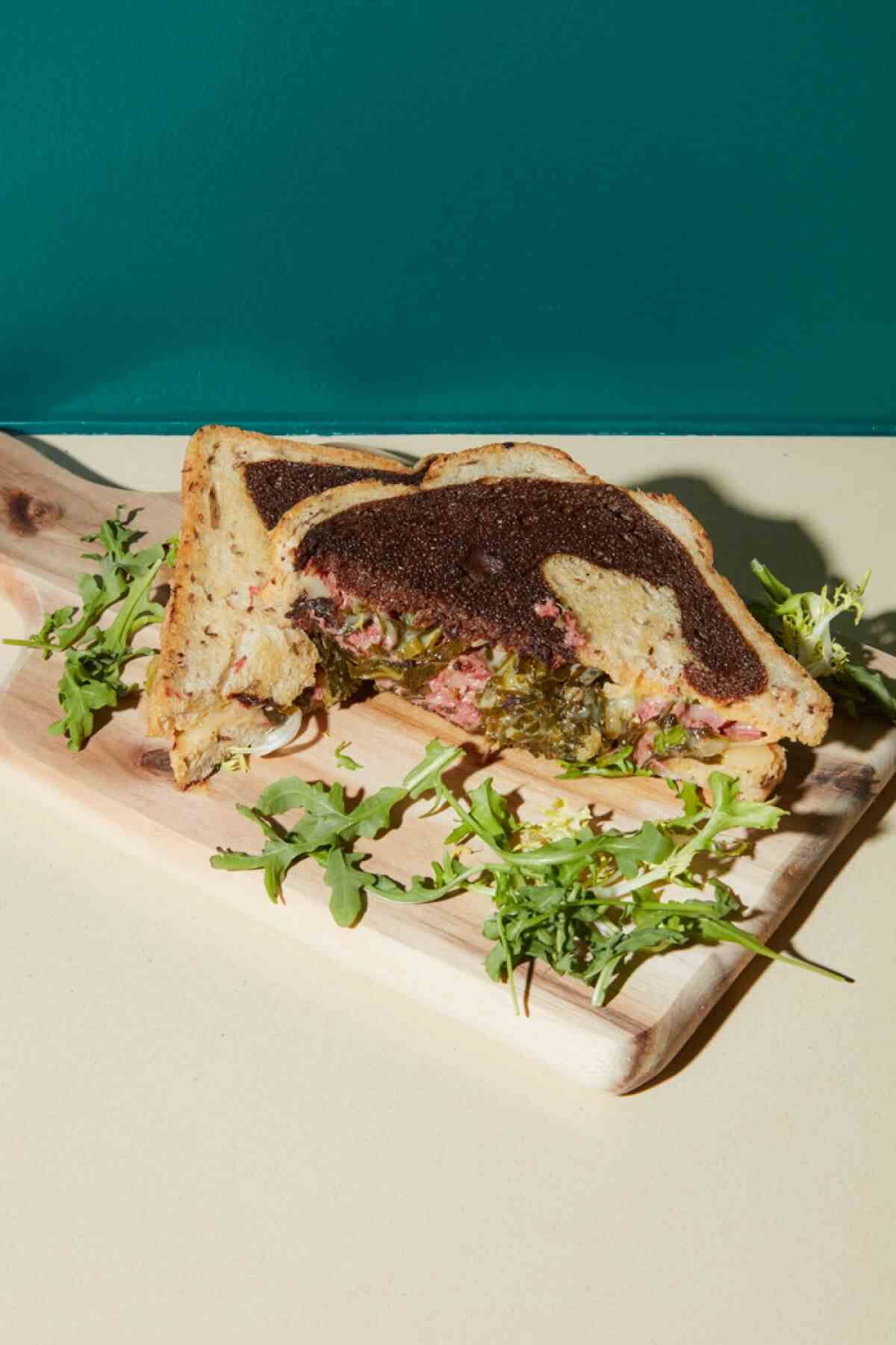 Ein Pastrami-Sandwich auf marmoriertem Roggen vor einer grünen Wand