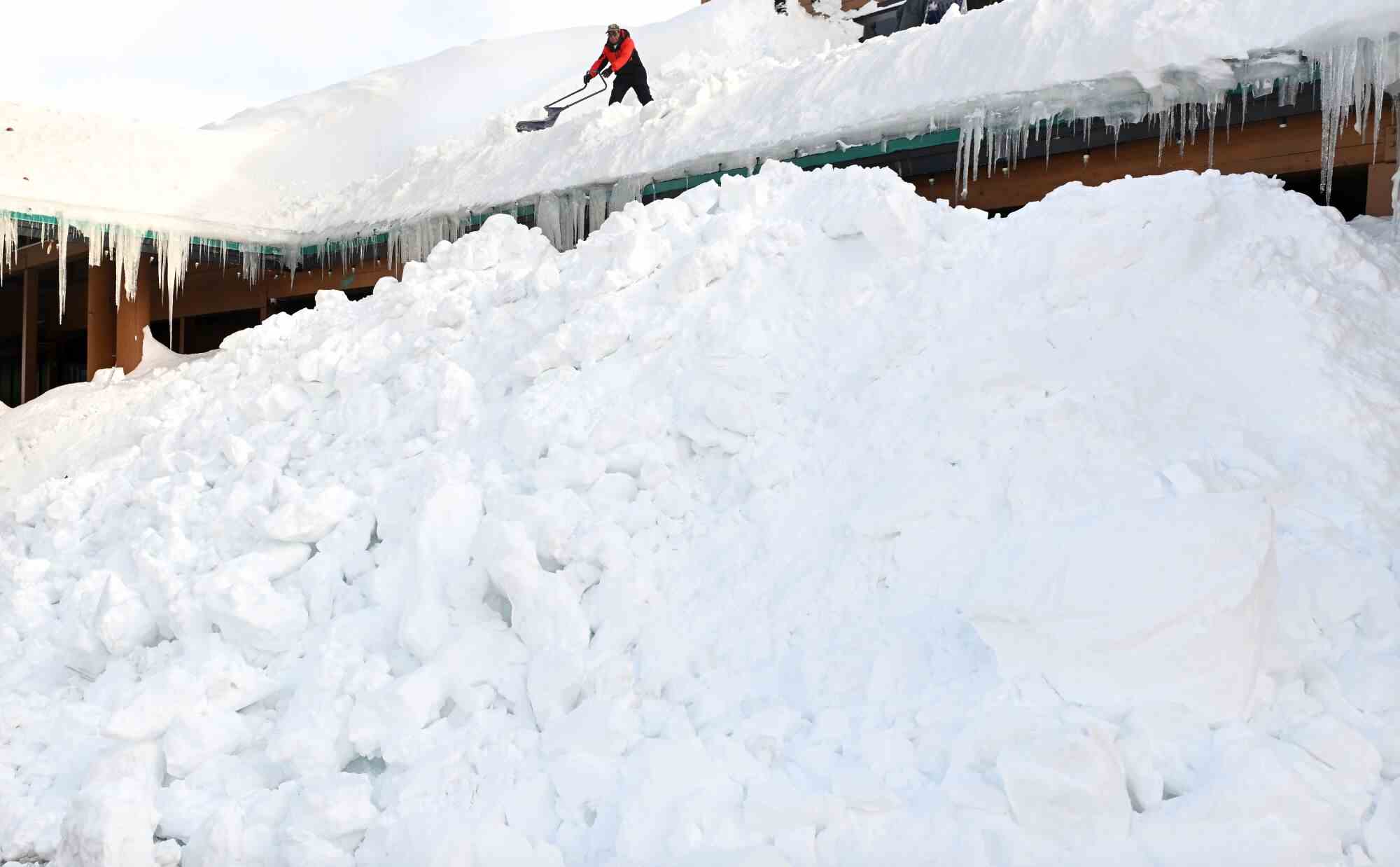 Ein Arbeiter wirkt wie ein Zwerg, als er in Mammoth Lakes Schnee von einem Dach schaufelt.