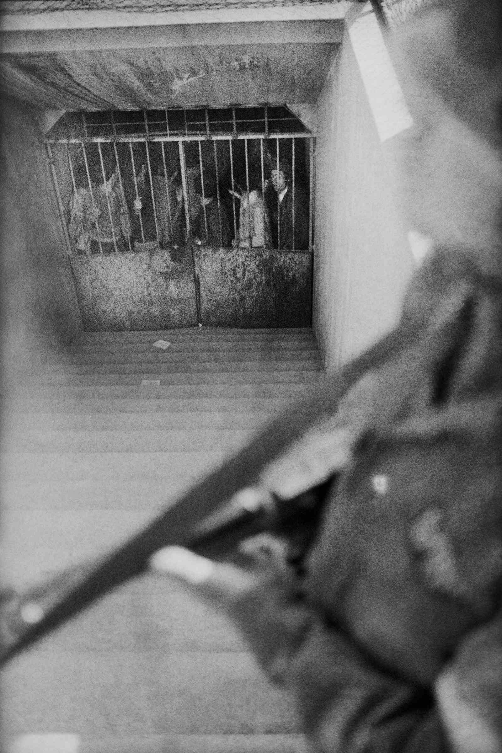 Ein Schwarz-Weiß-Foto eines bewaffneten Soldaten, der oben auf einer Treppe steht, die zu einer Menschenzelle führt.