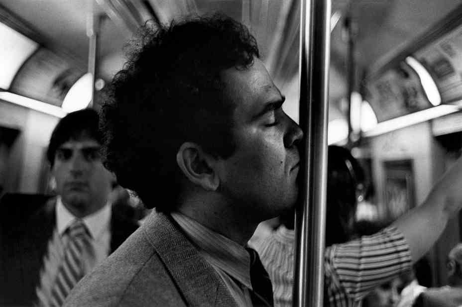 Ein Mann, der im Profil zu sehen ist, lehnt sein Gesicht gegen einen U-Bahnmast, während ein Mann im Hintergrund ihn ansieht.