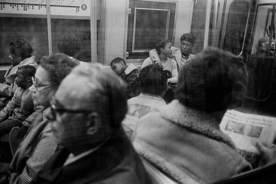 Passagiere in einem U-Bahn-Wagen durch das Fenster gesehen.  Ein Paar mit dem Arm des Mannes um die Frau schaut sich an.
