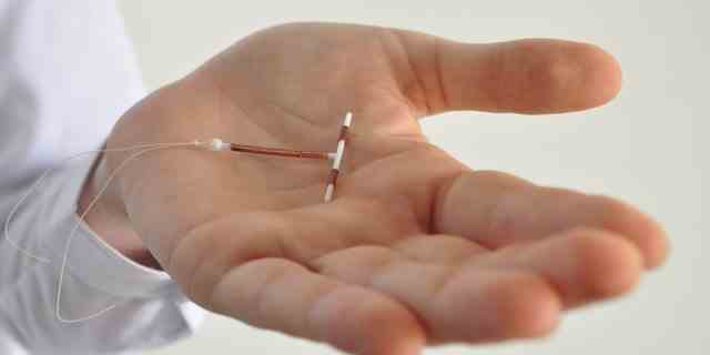 Hält ein Kupferspulengerät zur Empfängnisverhütung in der Hand - Seitenansicht