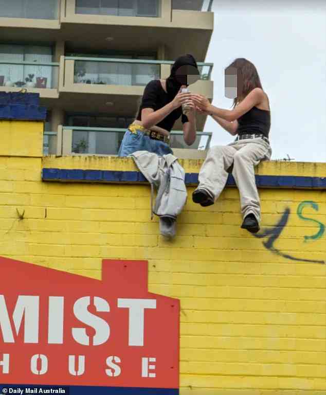 Zwei Mädchen im Teenageralter wurden auf dem Dach eines Gebäudes in einer belebten Stadtstraße fotografiert, während sie „eine Bong rauchen“ und Passanten zwischenrufen