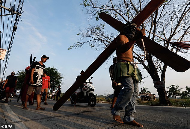 Ein katholischer Büßer trägt ein Holzkreuz, während er am Gründonnerstag in der Provinz Bulacan nördlich von Manila auf den Philippinen durch die Straßen geht, 06.04.2023