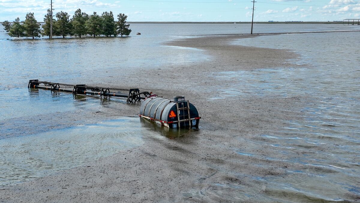 Ein Glanz auf der Oberfläche des Hochwassers, das halb untergetauchte landwirtschaftliche Geräte und einen Fasstank umgibt