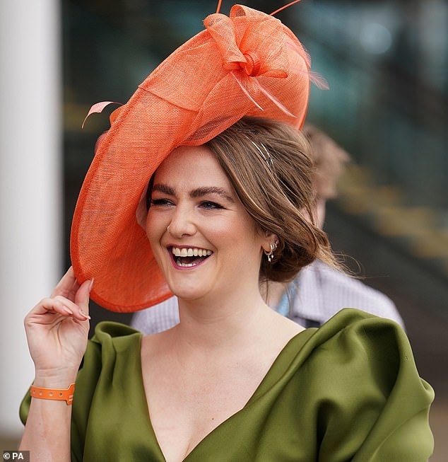 A winning smile! This elegant racegoer beamed as she held onto her orange hat, which she paired with a satin green dress with puffed shoulders