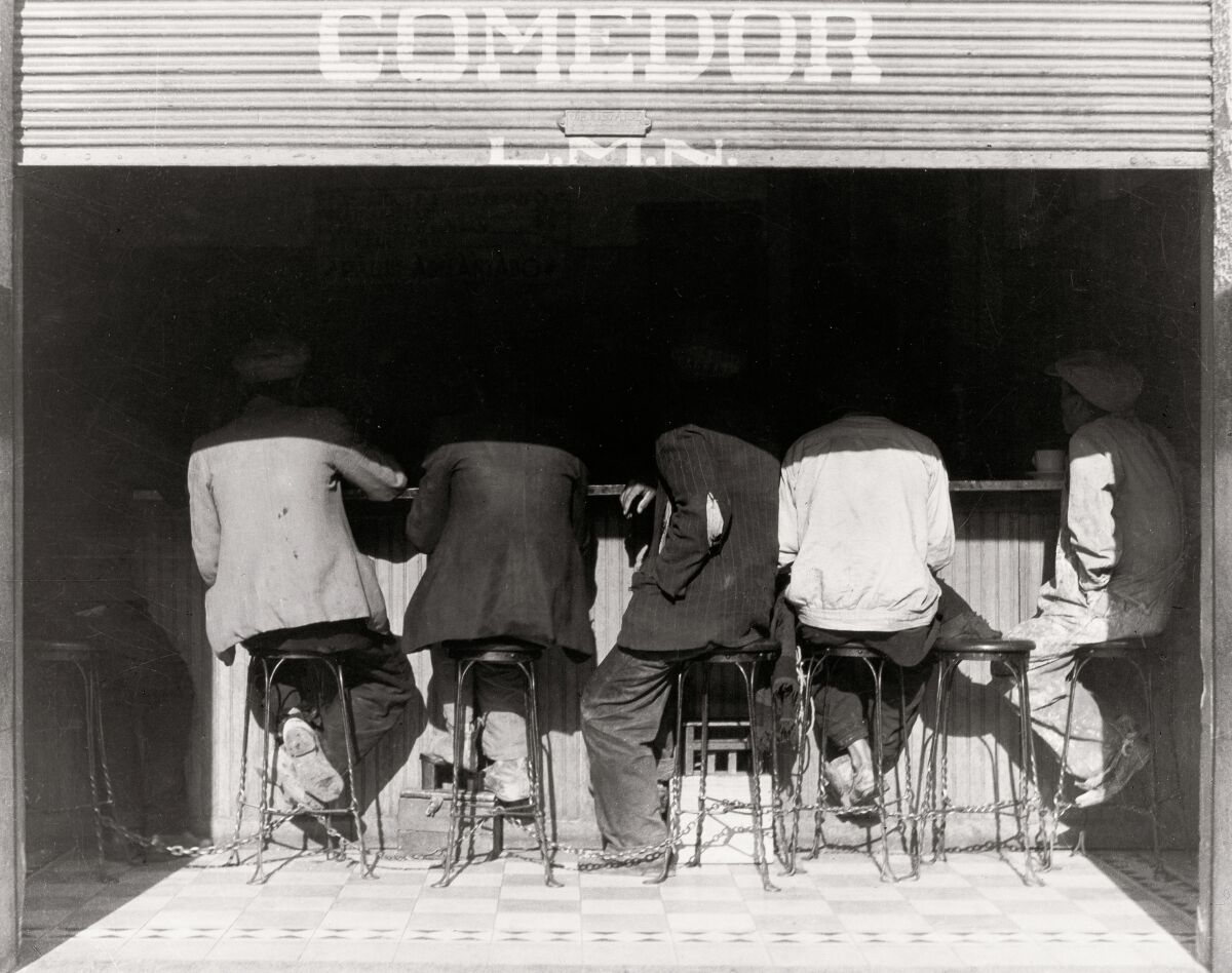 Ein Schwarz-Weiß-Bild von Menschen, die auf Hockern an einer Theke sitzen, von hinten gesehen