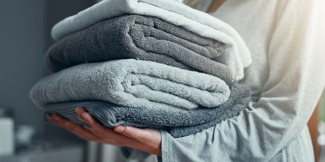 Nahaufnahme einer nicht erkennbaren Frau, die einen Stapel Handtücher trägt, während sie zu Hause Wäsche wäscht