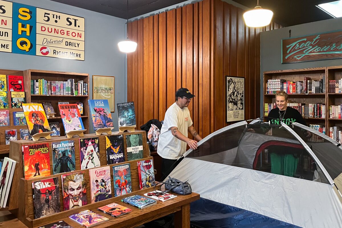 Zwei Personen bauen in einem Buchladen ein Zelt auf.