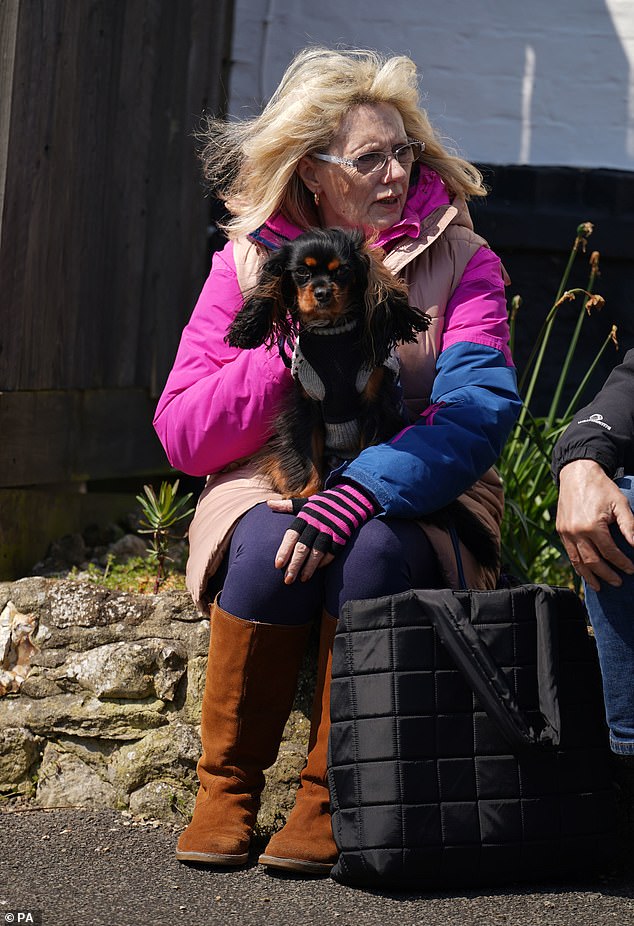 A Paul O'Grady fan sits on a stone wall with her dog in her lap as she awaits the funeral cortege of the late TV icon in Adlington, Kent