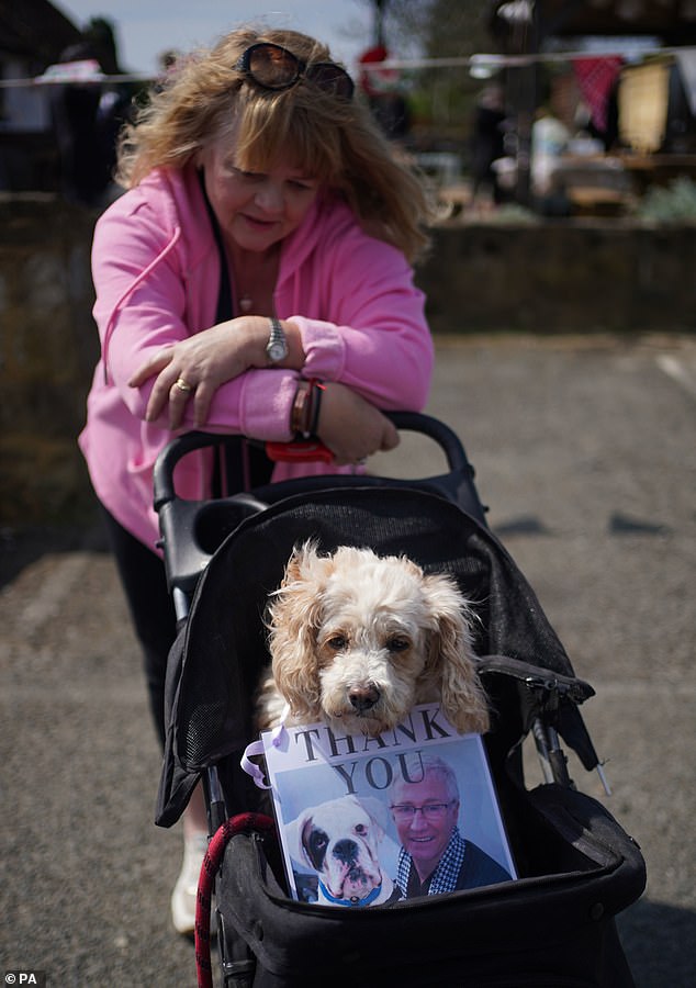 A fan waits outside the Walnut Tree Pub in Aldington, Kent, with her dog in a pram holding a 'thank you' sign, ahead of the cortege for Paul O'Grady travelling past on the way to his funeral at St Rumwold's Church