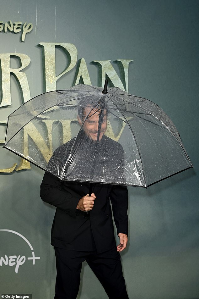 Einweichen: Der Star posierte mit seinem Regenschirm für ein lustiges Foto, als er gegen das Wetter ankämpfte