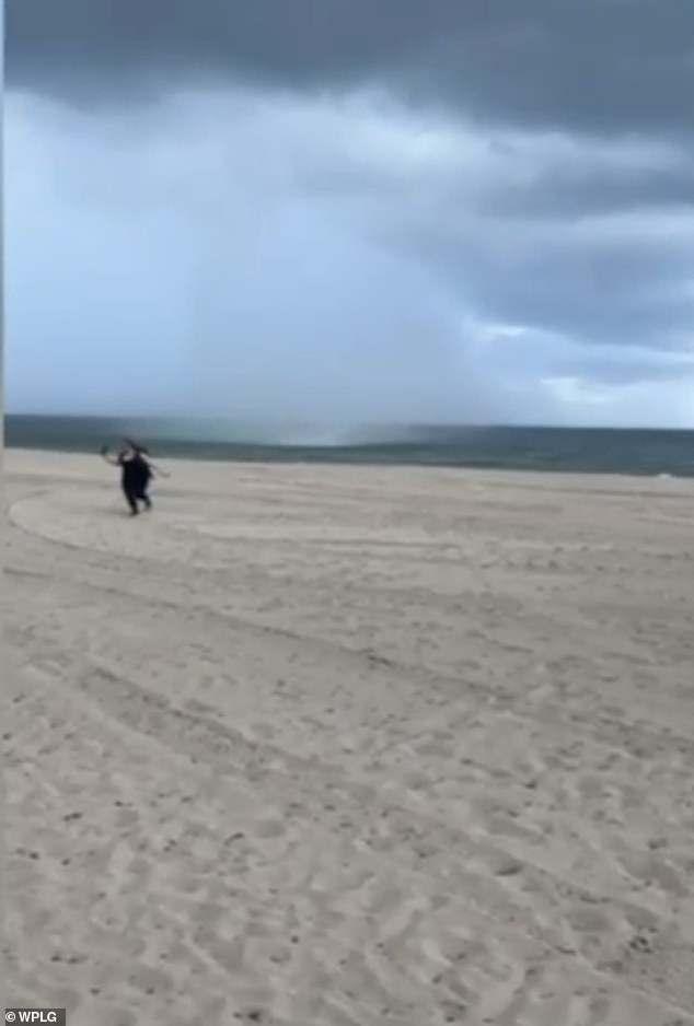 Eine Frau rennt über den Strand, während die Wasserhose ein paar Meter hinter ihr peitscht