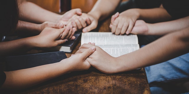 Leute, die Hände im Gebet um die Bibel halten