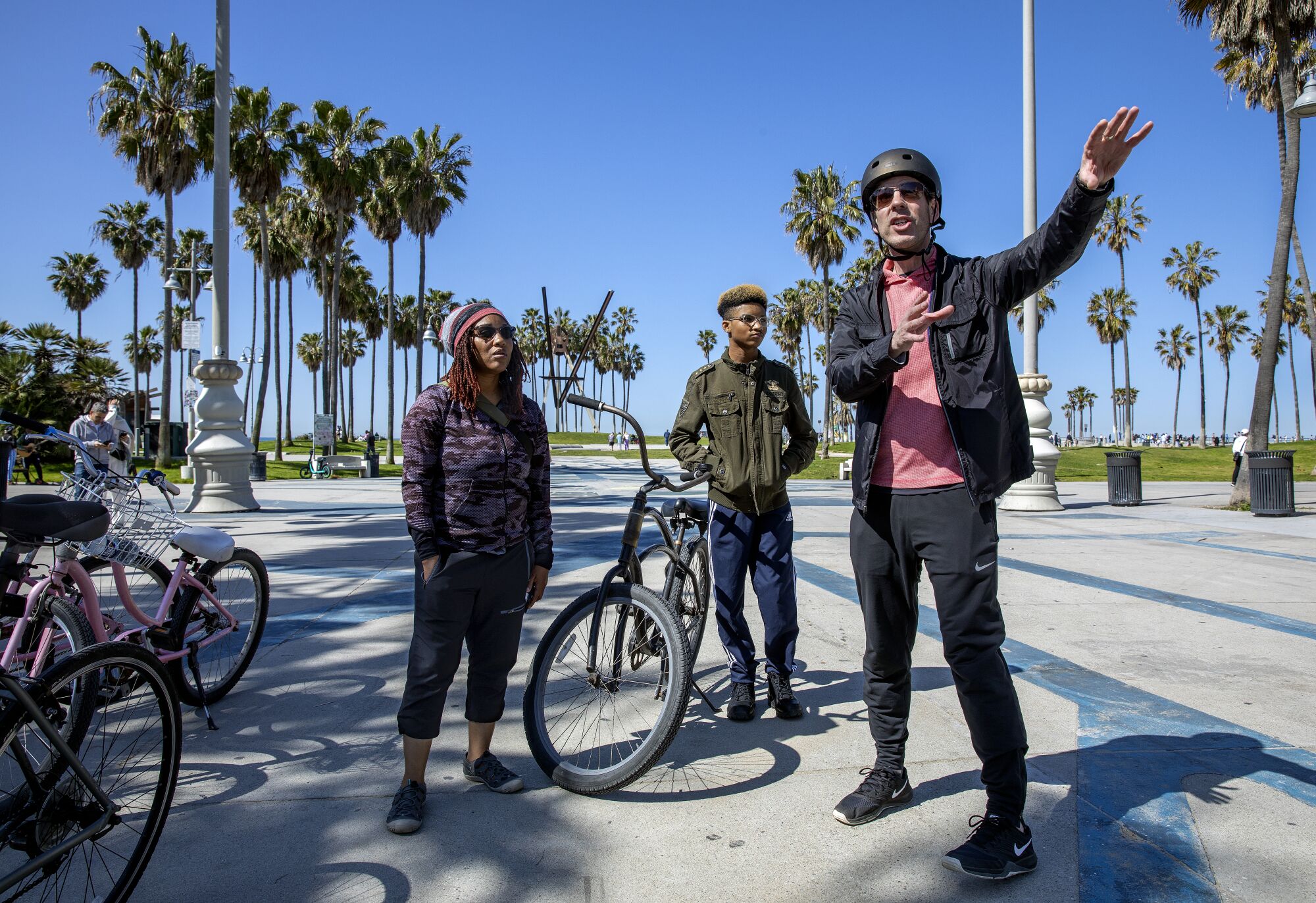 Ein Mann, rechts, hält am Venice Beach an, während er einer Frau und ihrem Sohn eine Tour gibt.
