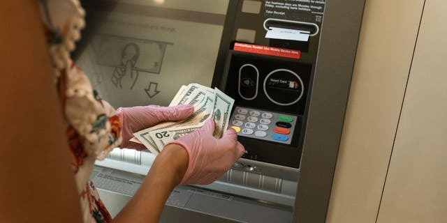 Frau mit Bargeld vor einem Geldautomaten