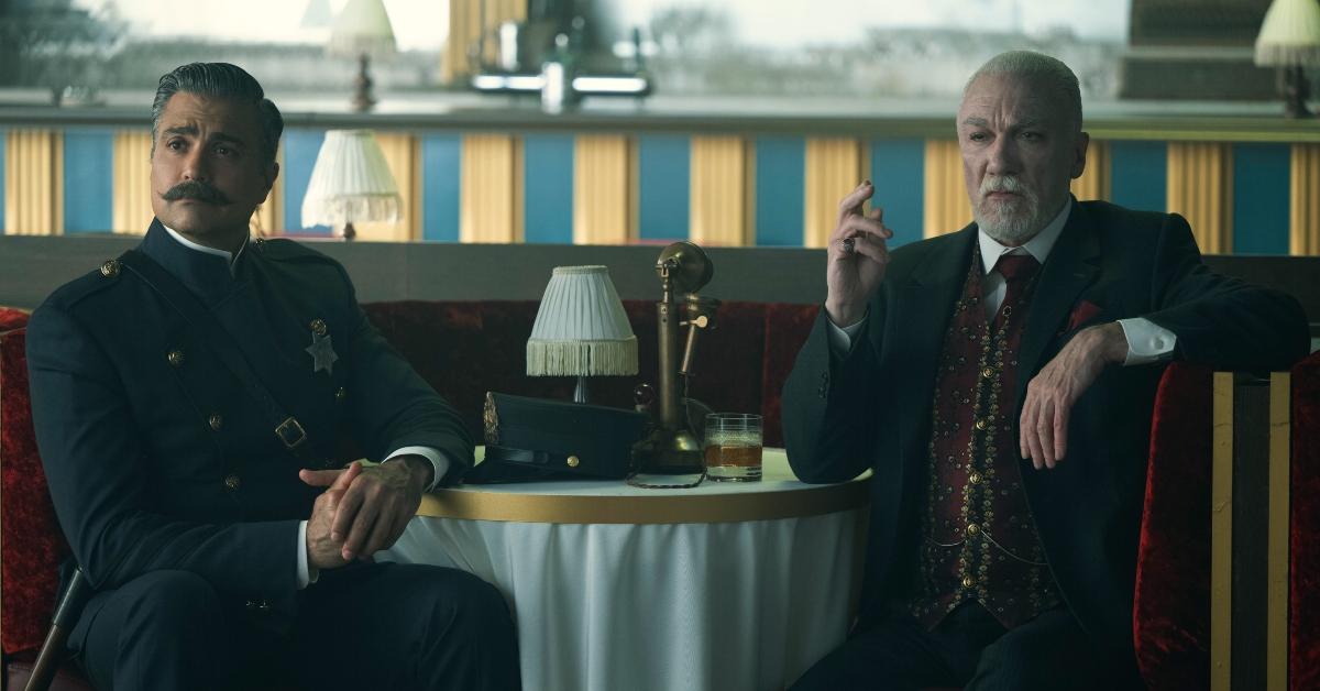 Jaime Camil als Sergeant Rivera und Patrick Page als Octavius ​​Kratt sitzen im Kratt-Club und schauen hinterhältig auf „Schmigadoon“. 