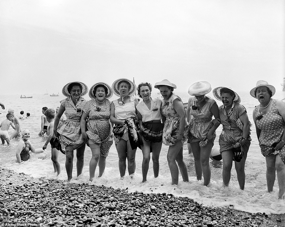 Pictured: A group of eight middle aged women go for a paddle with their hats on in the cold sea at Southend in July 1957