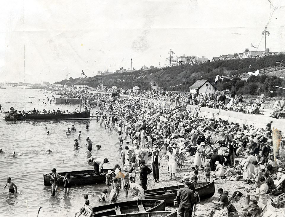 Pictured: Holidaymakers on a crowded West Beach with wooden boats at Clacton, Essex, in 1936