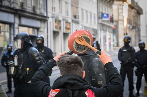 Ein Demonstrant schlägt während einer Demonstration am 24. April 2023 neben der französischen Polizei in Kampfausrüstung auf eine Pfanne