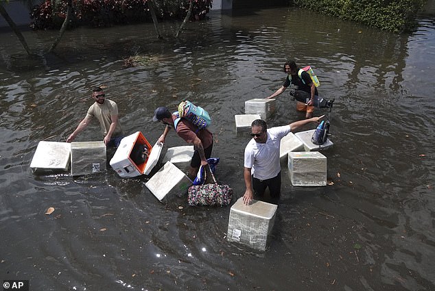 Menschen versuchen, Wertsachen zu retten, während sie am 13. April 2023 im Stadtteil Edgewood in Fort Lauderdale, Florida, durch Hochwasser waten